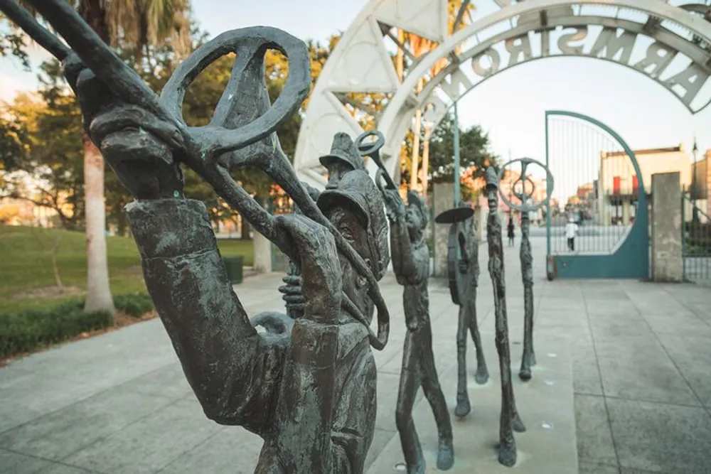 The image shows a series of bronze statues of jazz musicians capturing the essence of a vibrant music scene set against a park backdrop with an ornate gate in the distance