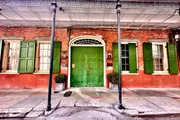 The image shows a vibrant street view featuring a historic red brick building with a green entrance door and matching green shutters accentuating its classical architectural details.