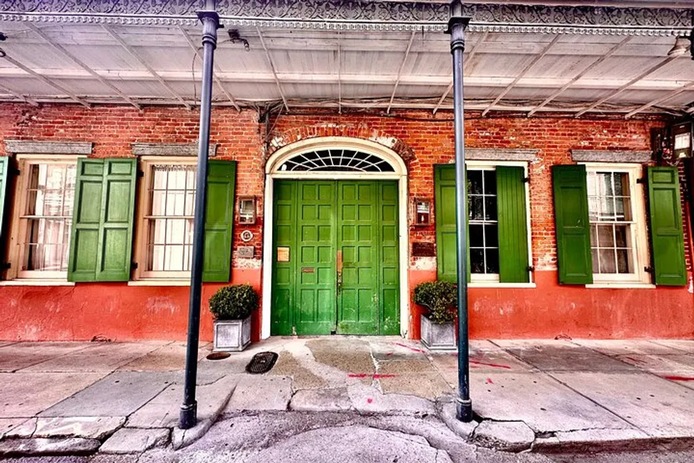 The image shows a vibrant street view featuring a historic red brick building with a green entrance door and matching green shutters accentuating its classical architectural details