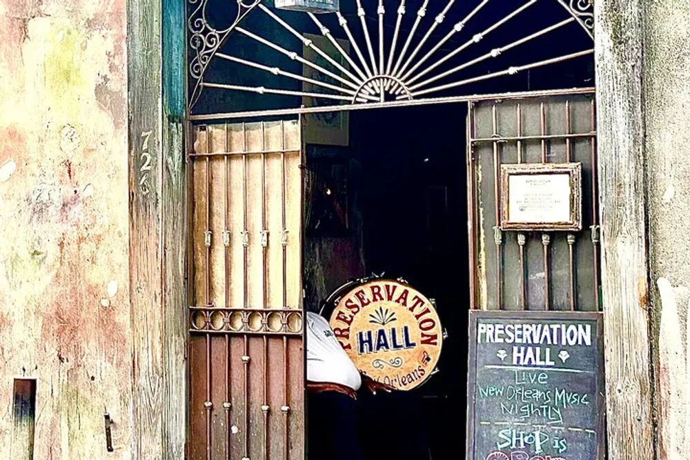 The image shows the entrance to Preservation Hall adorned with a weathered sign and an open door suggesting a welcoming passage to live music in New Orleans