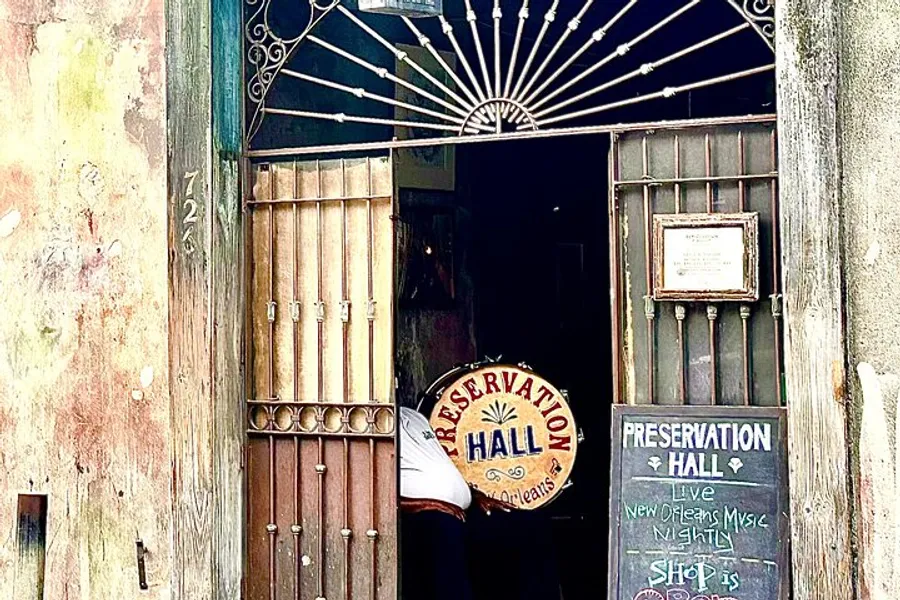The image shows the entrance to Preservation Hall, adorned with a weathered sign and an open door, suggesting a welcoming passage to live music in New Orleans.