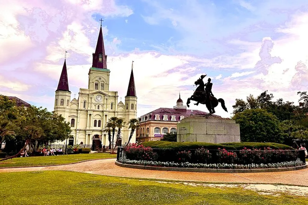 The image shows a historic cathedral with twin spires in the background and an equestrian statue in the foreground set against a backdrop of clouds and greenery in what appears to be a well-maintained urban park
