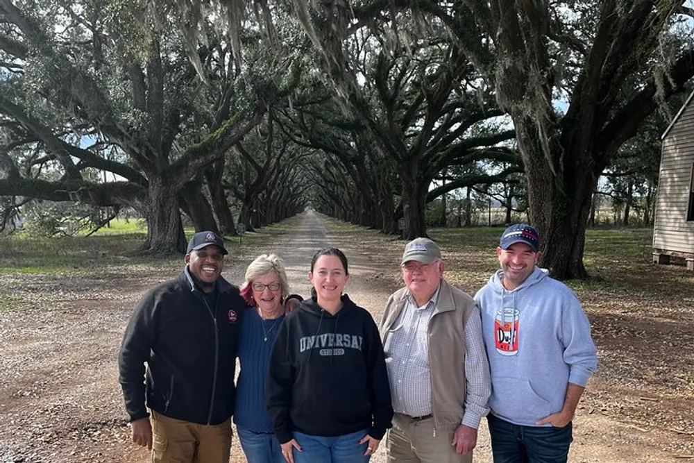 Five people are posing with smiles for a group photo in front of a scenic tree-lined dirt road