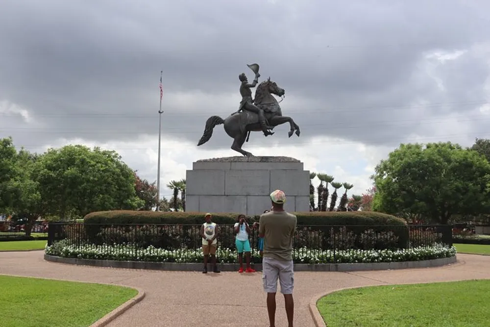 Visitors are looking at an equestrian statue in a park with manicured greenery and a cloudy sky overhead