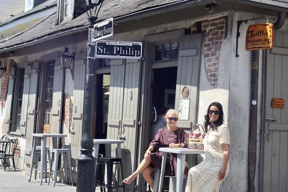 Two women are seated at an outdoor table near the corner of Bourbon and St Philip streets enjoying a sunny day