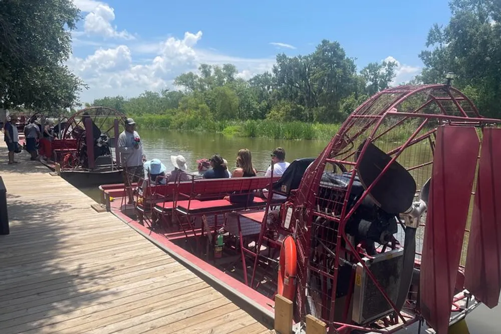 People are seated on an airboat tour preparing to explore a waterway lined with lush greenery under a sunny sky