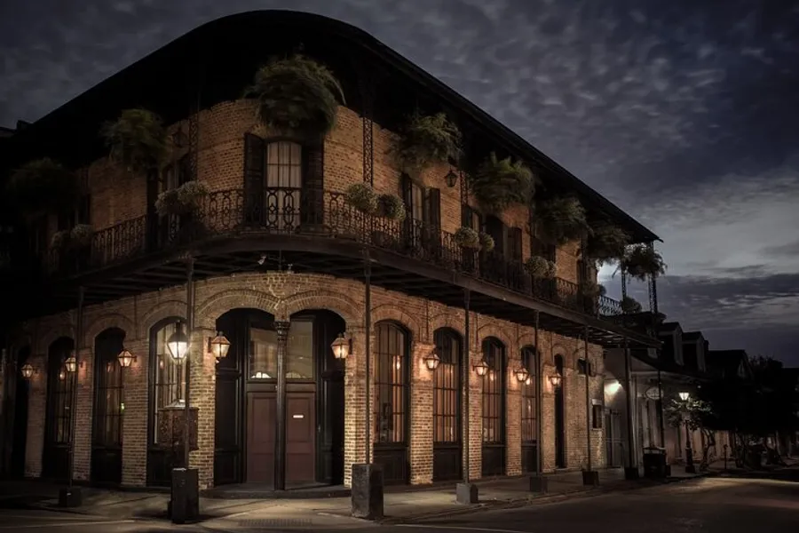 The image depicts a dimly lit, atmospheric corner of a brick building with a balcony adorned with plants, reminiscent of a tranquil evening in the French Quarter of New Orleans.