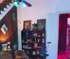 The image depicts a dimly lit room with eclectic decor featuring colored lights a high-back armchair a dresser with decorative objects and a lamp casting a blue glow near a window with green light coming through