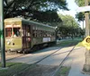 A vintage green and cream streetcar travels down a track-lined street next to a Look Both Ways sign and under the shade of trees with the street sign showing Eighth