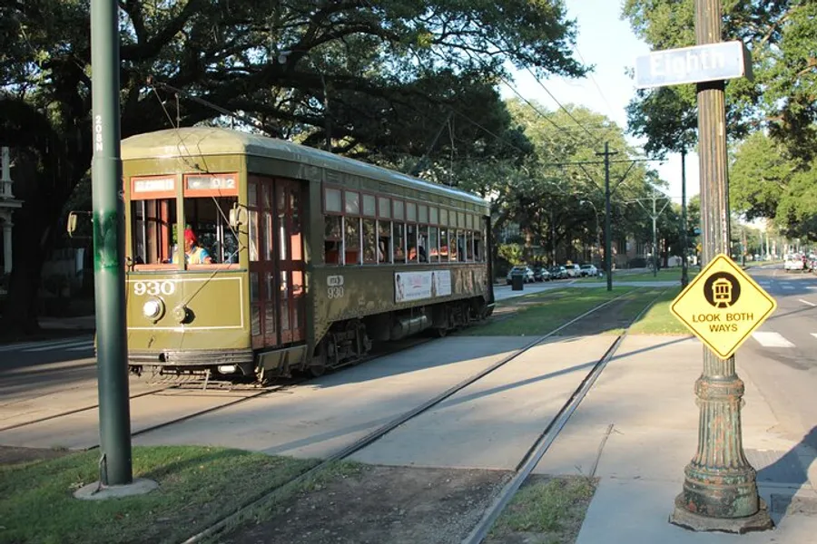 A vintage green and cream streetcar travels down a track-lined street next to a Look Both Ways sign and under the shade of trees, with the street sign showing Eighth.