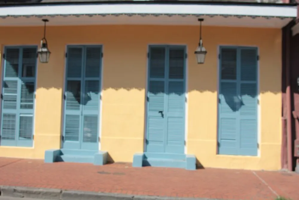 The image shows a yellow building with blue shutters on the windows and two hanging lanterns taken in bright daylight