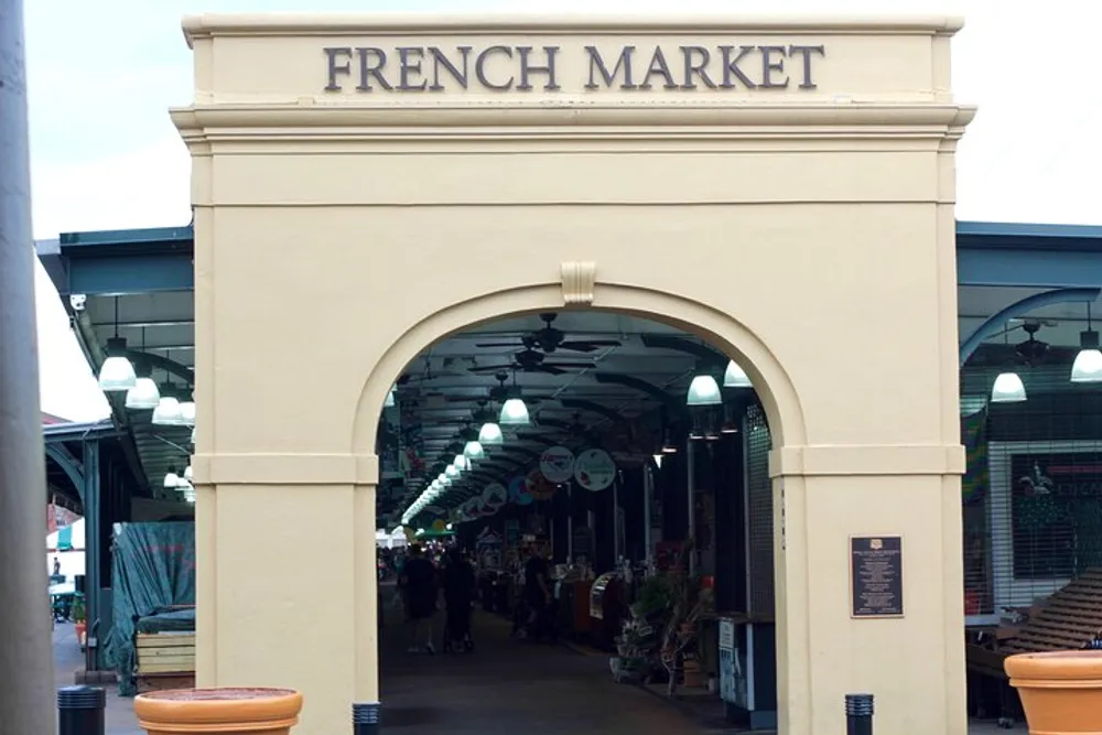 The image shows an arched entrance with the words FRENCH MARKET leading to a covered market alley with shops and people
