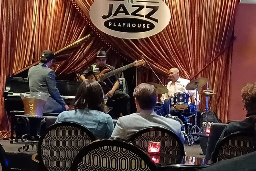 A trio of musicians perform live on stage at an intimate jazz club while an audience enjoys the ambiance