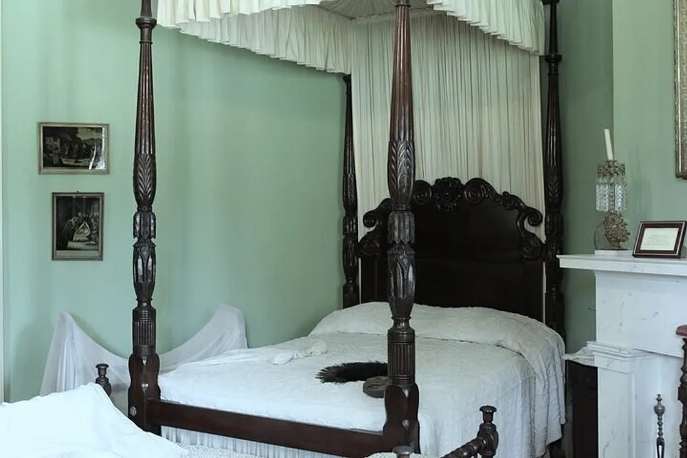 An antique four-poster bed with intricate wooden details in a room with light green walls and vintage dcor elements