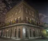 The image features a corner view of a historic two-story building at night with a classic wrought-iron balcony and deserted streets suggesting a quiet possibly eerie atmosphere
