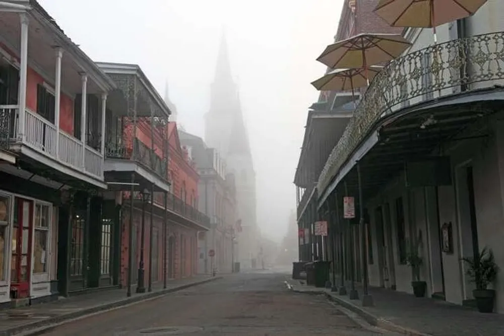 A foggy morning shrouds a street in the French Quarter of New Orleans with its historic architecture and a church spire fading into the mist