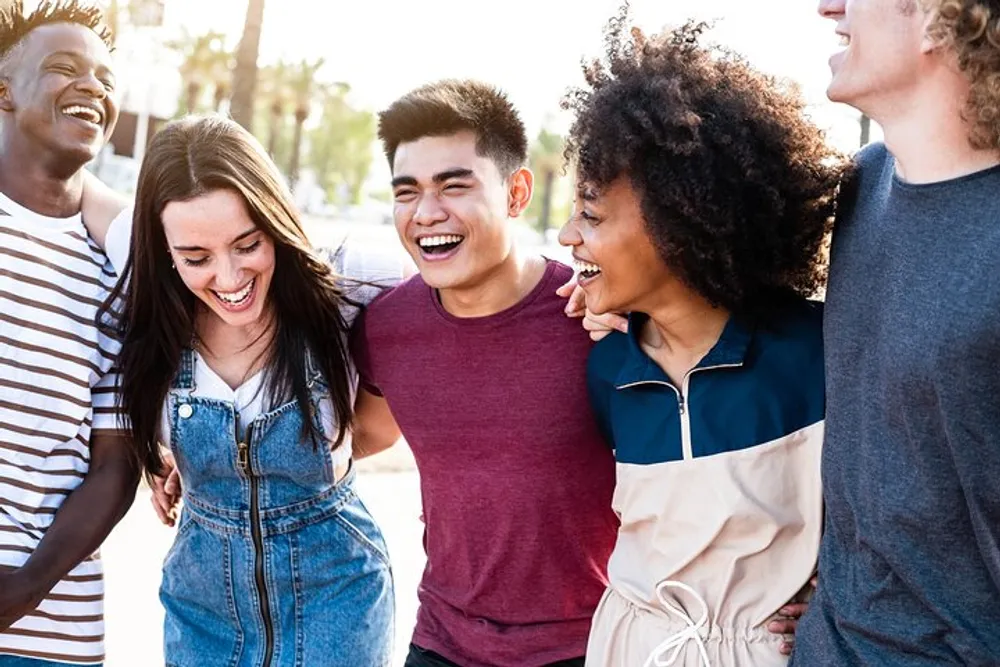 A diverse group of five cheerful young friends are laughing and having a good time together outdoors