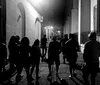 A group of people is walking down a narrow urban alleyway at night captured in a black and white photograph