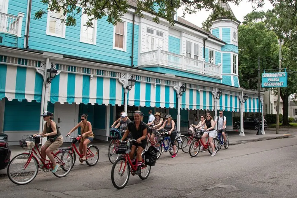 A group of people is cycling past a building with blue and white striped awnings on a tree-lined street