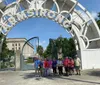A group of people are posing for a photo under a large decorative archway with the word ARMSTRONG on it in a sunny park setting