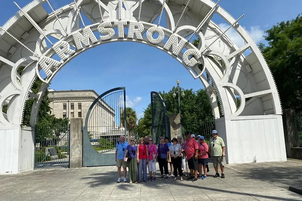 A group of people are posing for a photo under a large decorative archway with the word ARMSTRONG on it in a sunny park setting