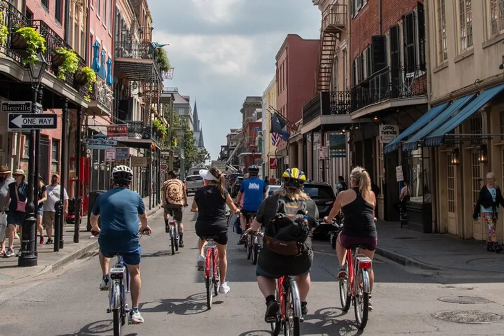 A group of cyclists is touring a sunny historic urban street lined with traditional buildings and balconies