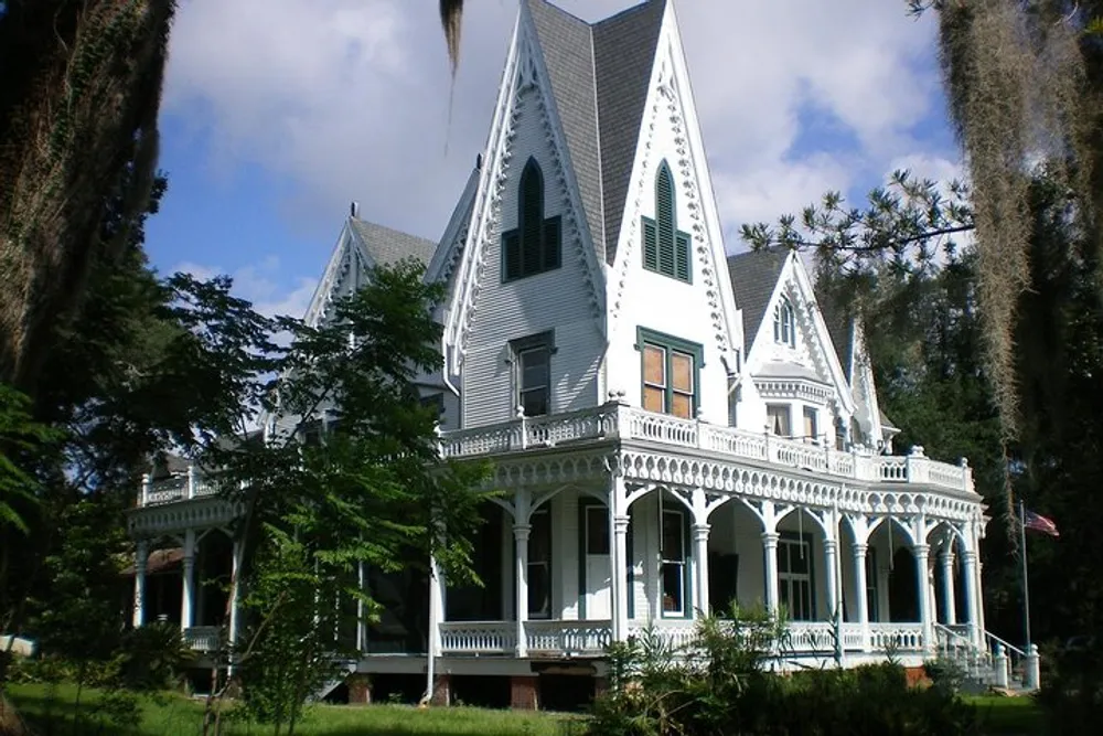 An ornate white Victorian-style house is adorned with intricate trim and surrounded by lush greenery