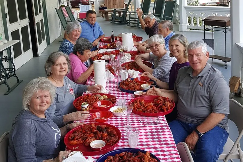 A group of people are enjoying a crawfish boil together at an outdoor table covered with a red and white checkered tablecloth