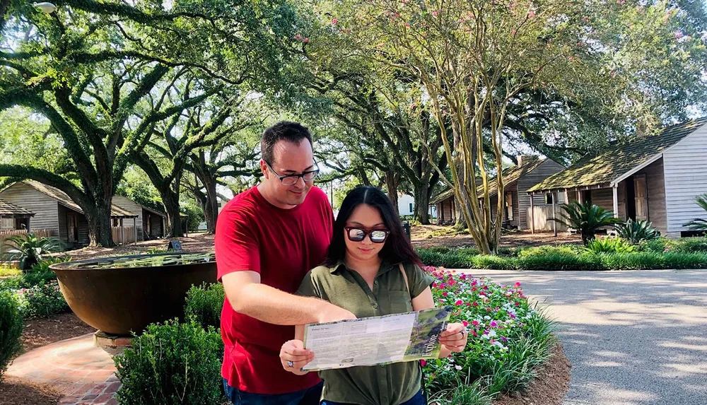 Two people are looking at a map or guide together in a lush garden with historic buildings in the background