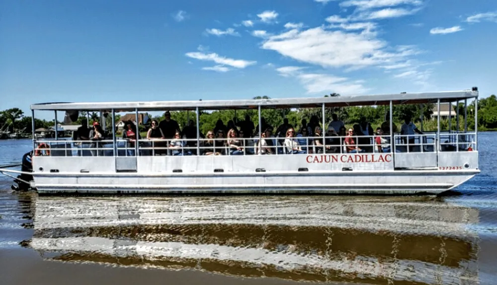 A group of people is enjoying a boat tour on a vessel named Cajun Cadillac cruising on a calm body of water under a clear sky
