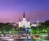 The image shows a twilight scene featuring the iconic St Louis Cathedral with a line of horse-drawn carriages in the foreground at Jackson Square in the French Quarter of New Orleans