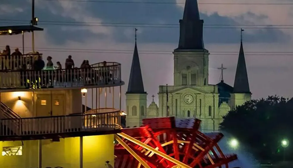 Visitors enjoy a scenic view from a balcony overlooking the New Orleans skyline highlighted by the illuminated St Louis Cathedral and a vibrant red paddlewheel