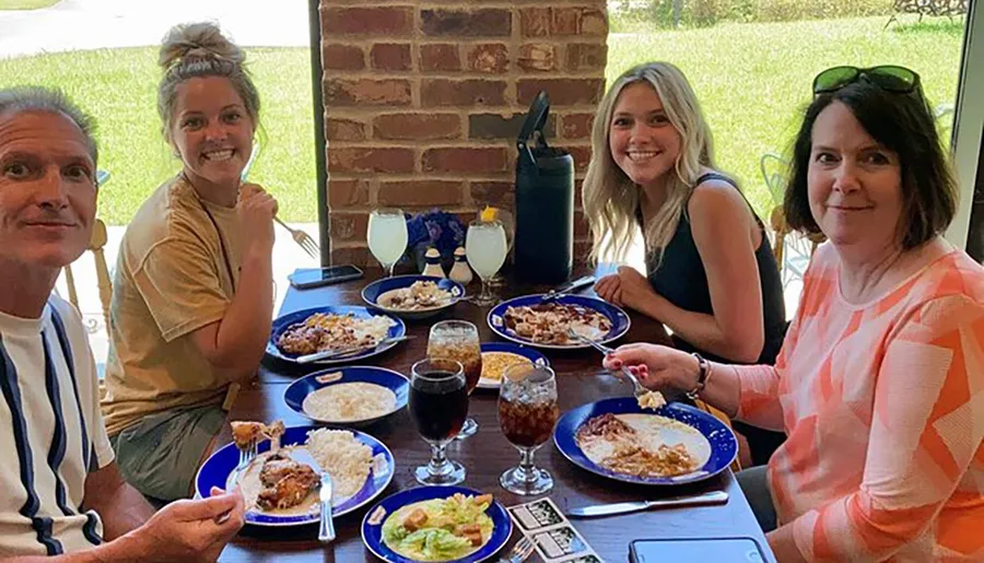 Four people are smiling at the camera while dining together at a table with plates of food and drinks.