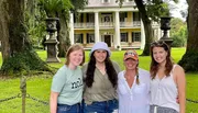 Four people are smiling for a photo in front of a classic two-story house with large columns and surrounded by trees.