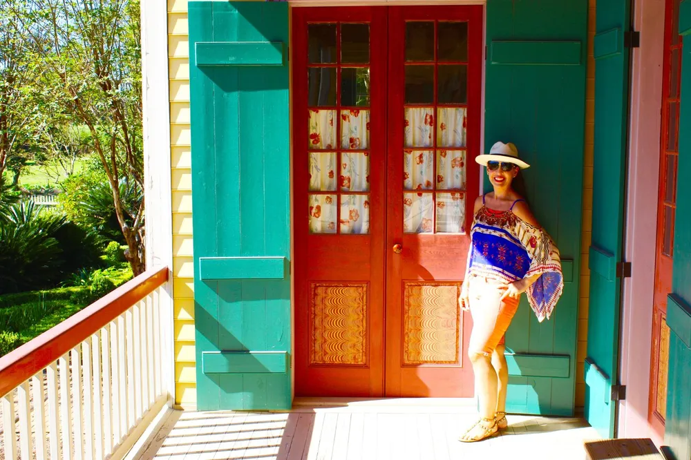 A person is standing by a brightly colored doorway smiling and posing for the camera on a sunny day