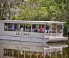 A group of people are enjoying a boat tour on a flatboat named Lil Cajun through a tree-lined waterway