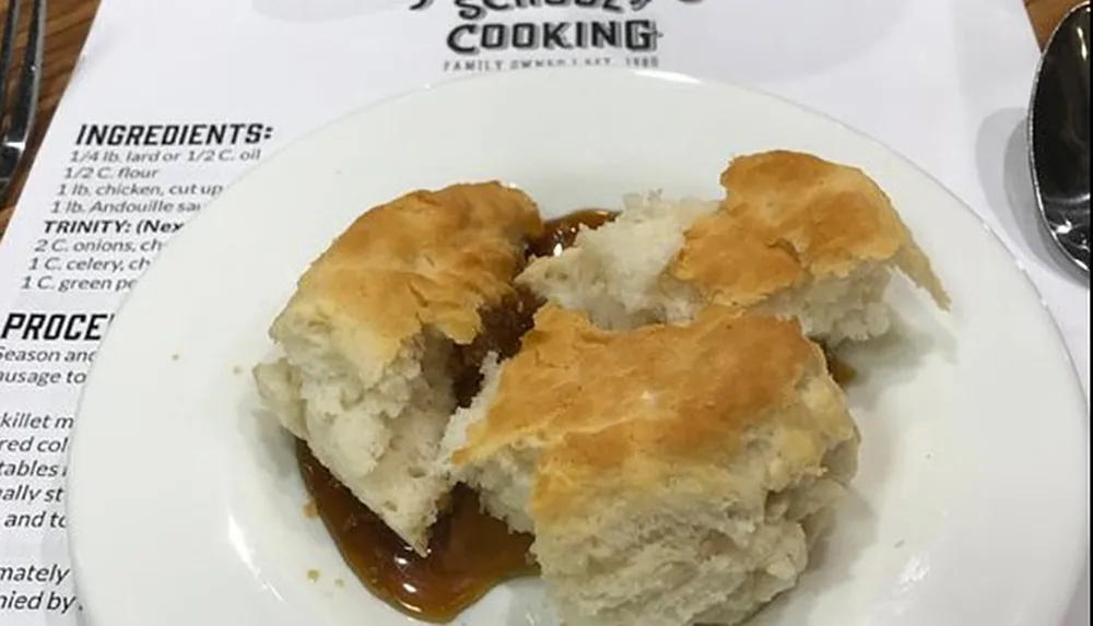 The image shows freshly baked biscuits on a plate with gravy next to a recipe sheet or book suggestive of a home cooking environment