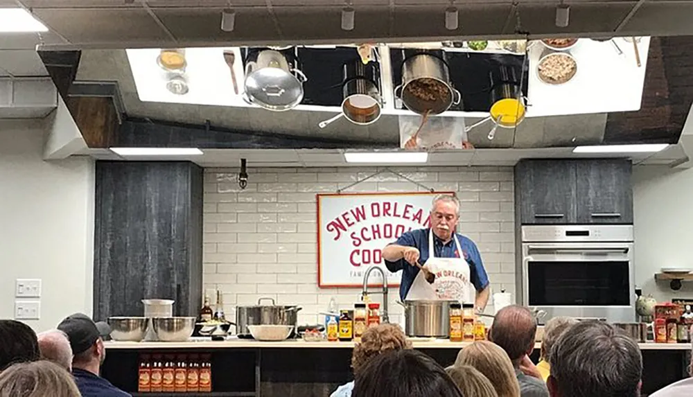 A chef is giving a cooking demonstration to an audience at the New Orleans School of Cooking