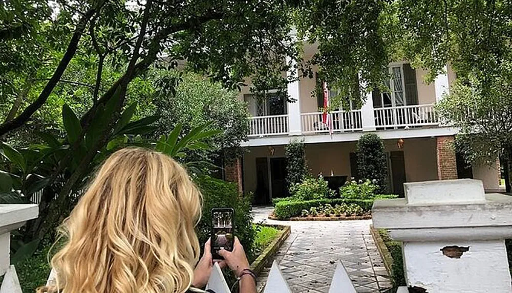 A person with blonde hair is taking a photo of a two-story building with a smartphone