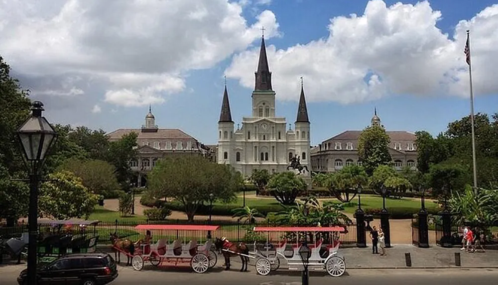 The image captures a sunny day at Jackson Square with the iconic St Louis Cathedral in the background a horse-drawn carriage in the fore and people enjoying the outdoors in New Orleans French Quarter