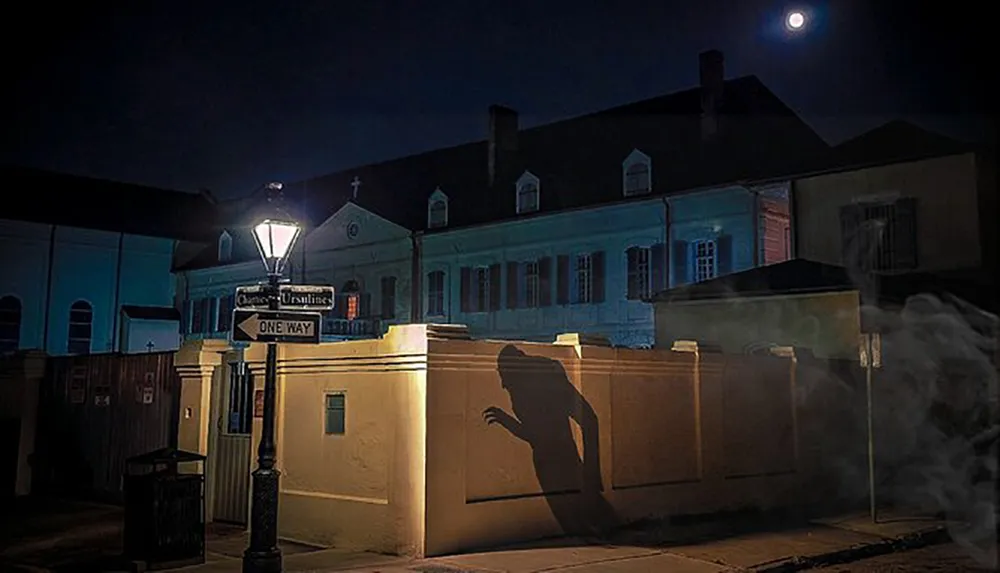 An eerie shadow resembling a person is cast on a wall beside a streetlight on an old town street at night evoking a ghostly atmosphere