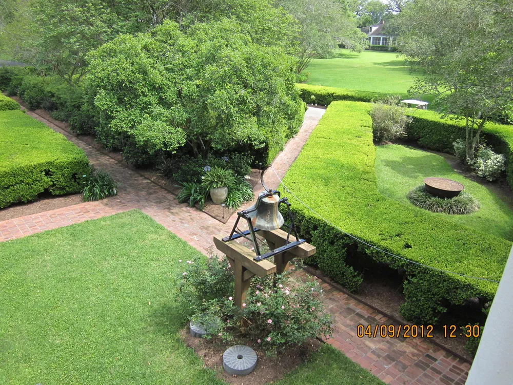 The image shows a well-manicured garden with geometric hedge layouts a brick pathway and a date stamp of 04092012 1230