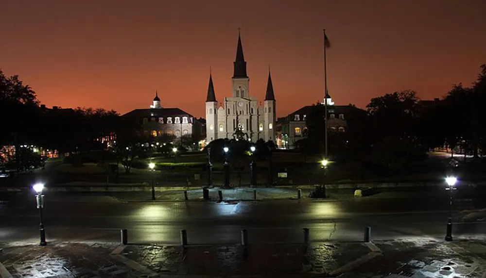 An evening view of Jackson Square with the historic St Louis Cathedral lit against an orange-hued sky in New Orleans