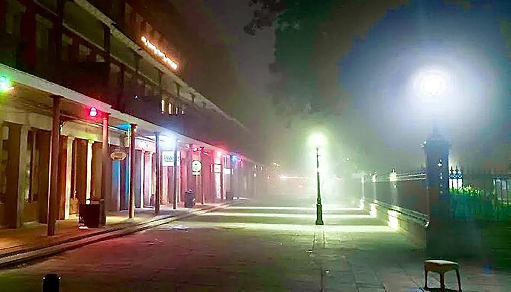 The image depicts a foggy urban street scene at night with colorful lights above the storefronts and a bright street lamp casting light through the mist