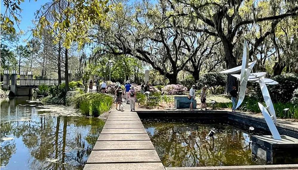 Visitors enjoy a sunny day at a scenic park with a reflective pond modern sculpture and Spanish moss-draped trees