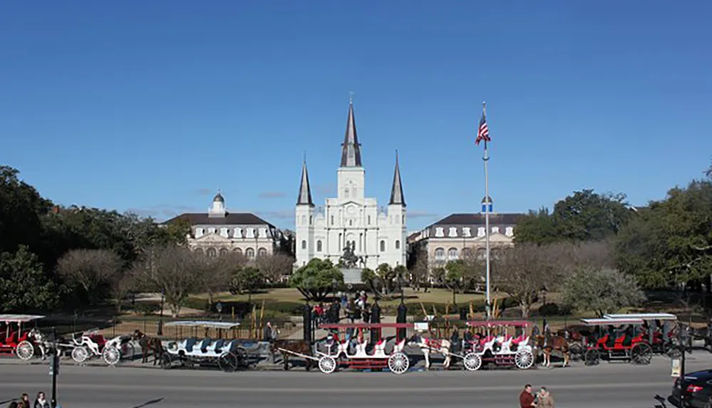 The image presents a sunny day view of Jackson Square in New Orleans with the St Louis Cathedral in the background and a line of horse-drawn carriages in the foreground