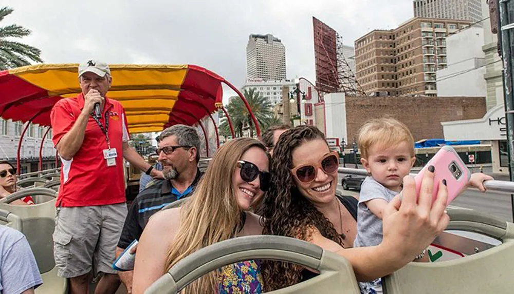 Two women are posing for a selfie with a young child on a sightseeing bus while a tour guide speaks into a microphone