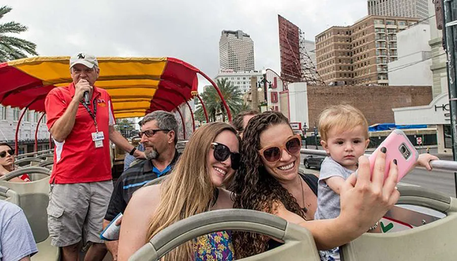 Two women are posing for a selfie with a young child on a sightseeing bus, while a tour guide speaks into a microphone.