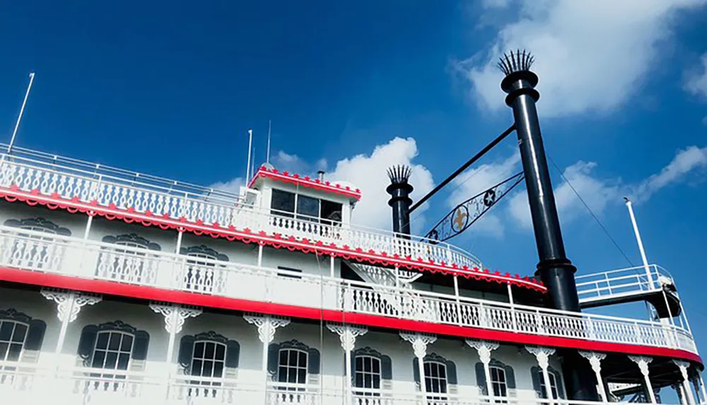 A paddle steamboat with iconic tiers and decorative railings is set against a bright blue sky with sparse clouds
