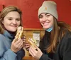 Two smiling women are holding up their sandwiches for the camera inside a casual dining establishment